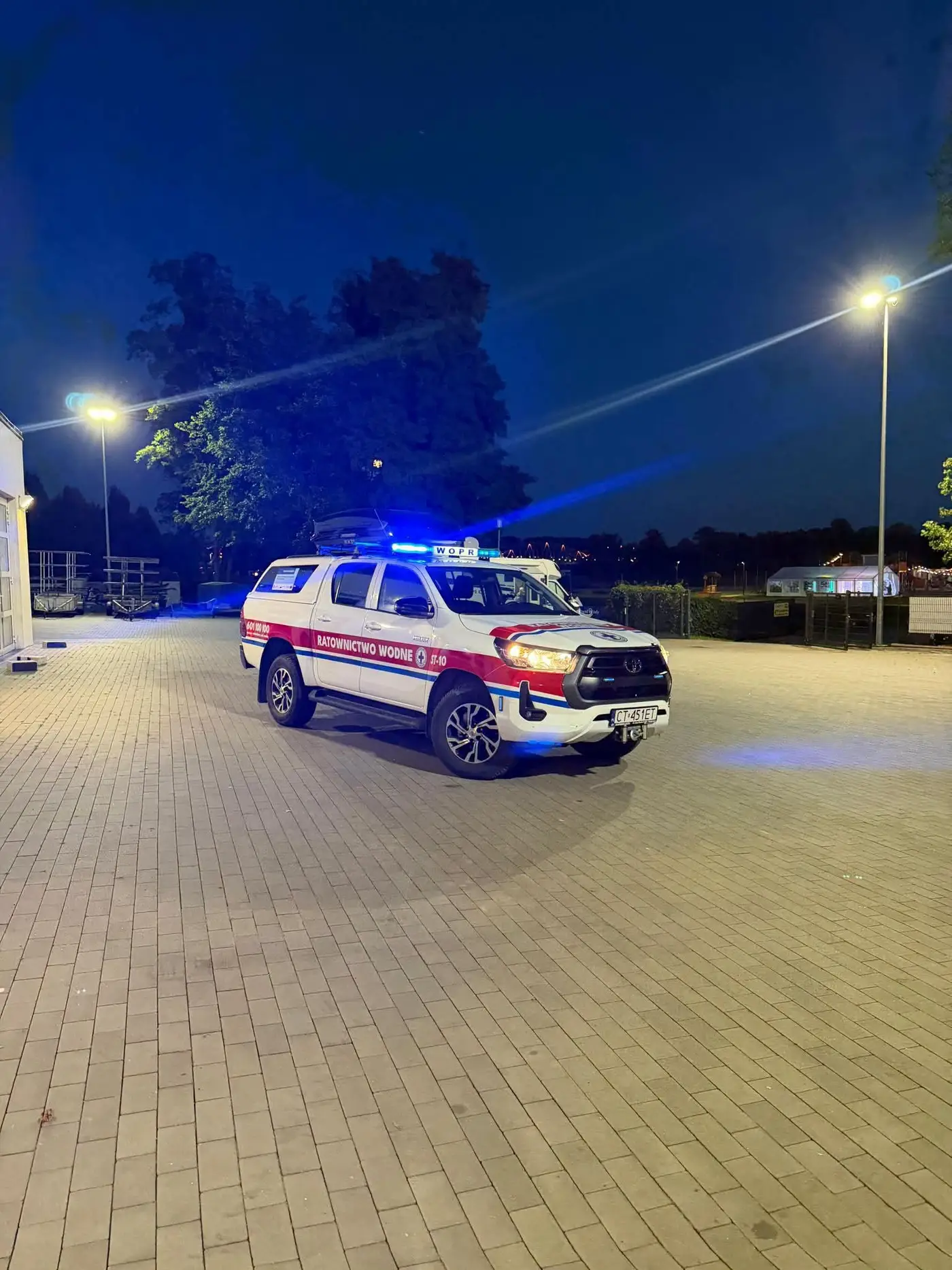 Pickup Toyota Hilux Ratownictwa Wodnego WOPR nocą na placu przy latarniach, z włączonymi sygnałami świetlnymi